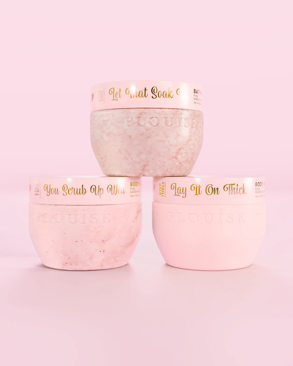 Τρία ροζ δοχεία P.Louise Hop Into Self-Care Pink Marshmallow με άλατα μπάνιου, απολέπιση σώματος και βούτυρο σώματος με χρυσό κείμενο σε ροζ φόντο