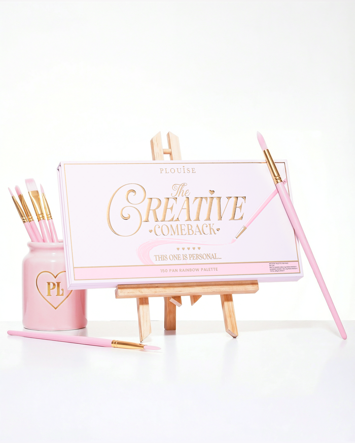 Μια κλειστή ροζ P.Louise Creative Comeback XXXL Rainbow Eyeshadow Palette τοποθετημένη σε ένα καλλιτεχνικό καβαλέτο που περιβάλλεται από πινέλα μακιγιάζ