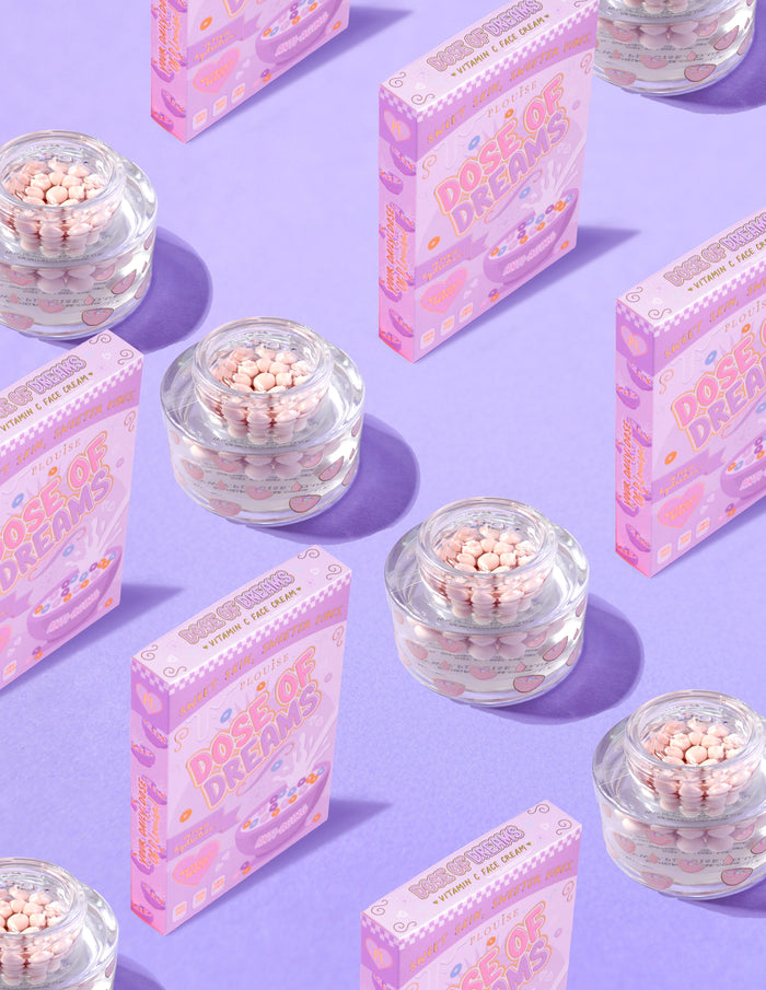 Διαφανή δοχεία P.Louise DOse of Dreams Viatmin C Capsule Face Cream με ροζ κάψουλα μέσα σε αυτά που περιβάλλονται από ροζ κουτιά δημητριακών σε μωβ φόντο