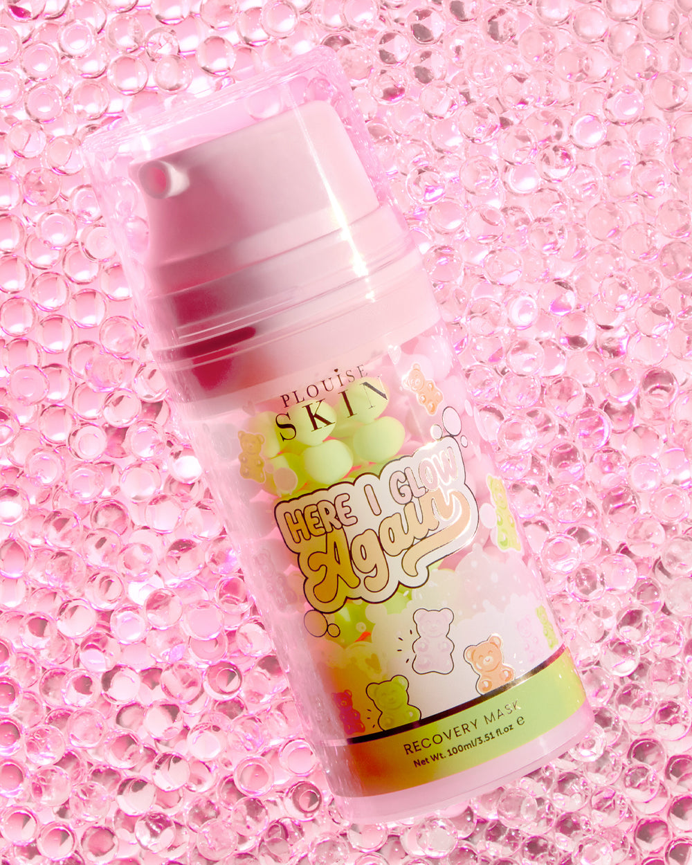 Ένα μπουκάλι P.Louise Here I Glow Again Recovery Mask σε αρκούδες καραμέλας με άρωμα με ροζ και πράσινη ετικέτα, με εικονογραφήσεις με αρκουδάκια, τοποθετημένα σε ροζ αστραφτερό φόντο.