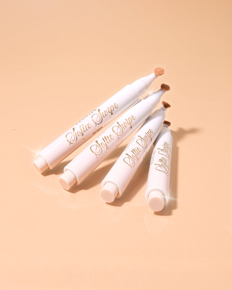 Μια εικόνα τεσσάρων P.Louise Softie Swipe Tinted Lip Masks με άρωμα κέικ καρύδας στοιβαγμένες μεταξύ τους με μπεζ φόντο