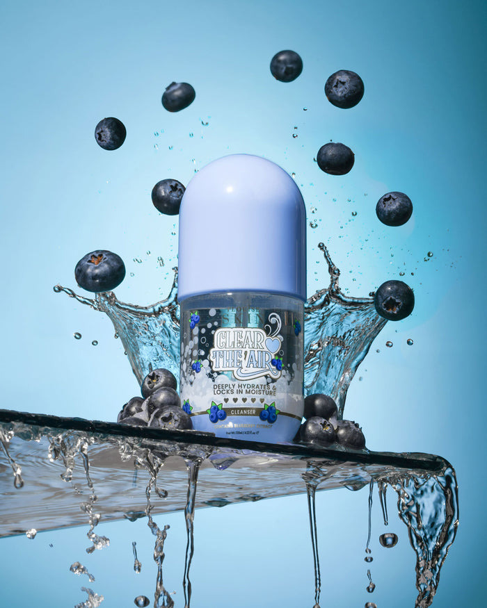 Μπουκάλι P. Louise Clear The Air Blueberry Gel Cleanserl που περιβάλλεται από βατόμουρα και πιτσιλιές νερού σε μπλε φόντο