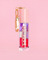 P. Louise Soak Me Lip Oil με πολύχρωμο λαδάκι σε ροζ σωλήνα με χρυσό κούμπωμα σε ροζ φόντο